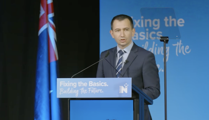 Pakuranga MP Simeon Brown speaking at a lectern carrying National Party branding