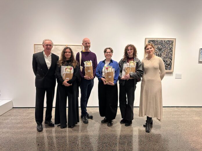 Six people standing in the Malcolm Smith Gallery at Uxbridge, four holding gift bags