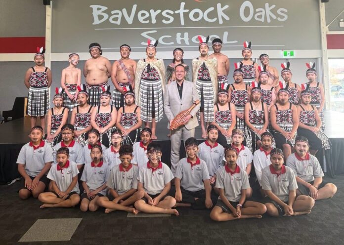Baverstock Oaks School principal Ian Dickinson holding a carved taonga among the school's kapa haka group in front of the school logo