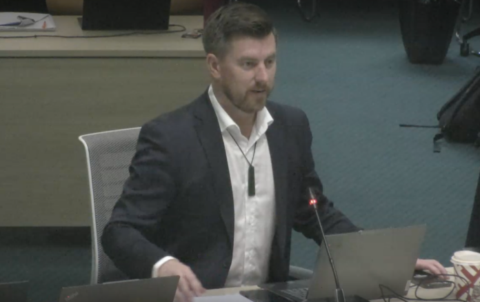 Auckland councillor Richard Hills speaking at a council meeting, seated at a desk with a microphone in front of him