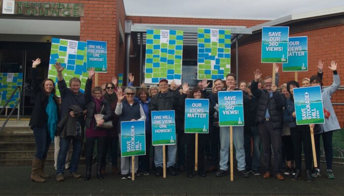 Members of the Save Stockade Hill lobby group waving and holding placards reading Save Stockade Hill Views, Our Views Matter and One Hill One View One Howick outside the Fencible Lounge in Howick in 2018