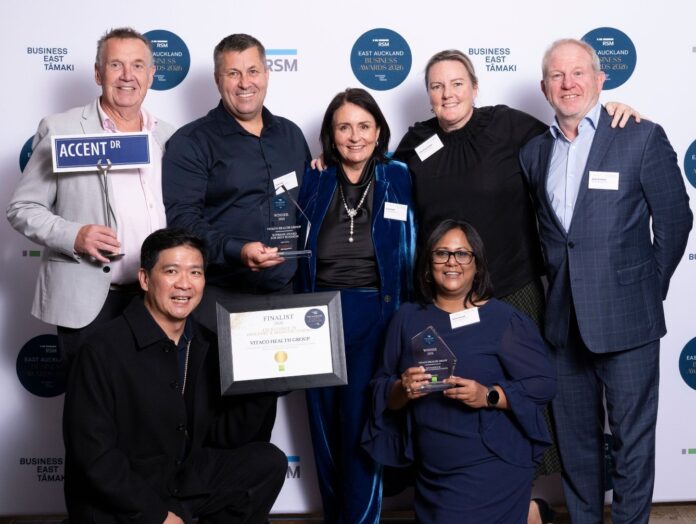 Vitaco Health Group staff holding trophies at the RSM East Auckland Business Awards media wall