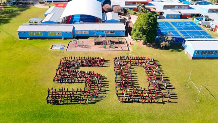 Aerial photograph of students in red uniforms standing in formation to spell the number 50 on Wakaaranga School's field