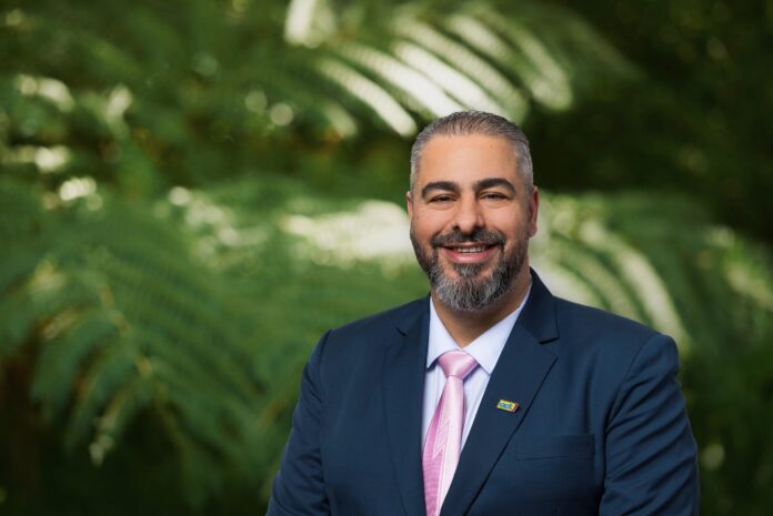Ali Dahche, ACT's candidate for Botany, in a navy suit and pink tie in front of ferns