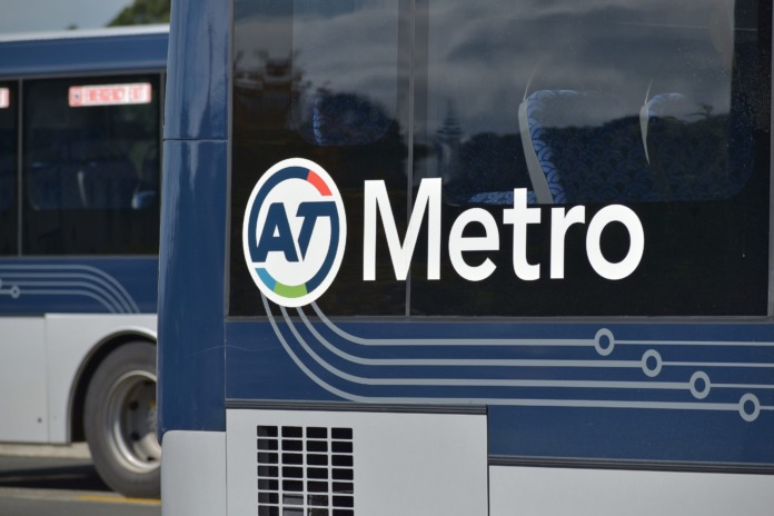 The rear corner of a dark blue Auckland Transport bus showing the AT Metro logo and wordmark, with a second bus behind it.
