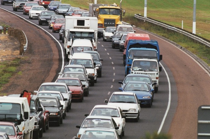 Two lanes of stationary traffic nose to tail on a motorway, seen from above, with an empty shoulder alongside.