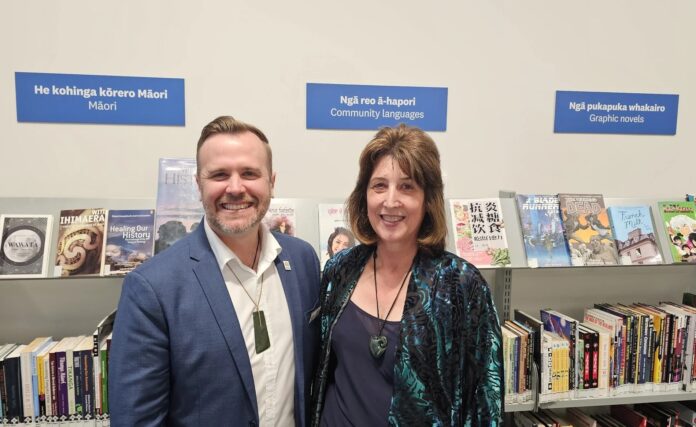 Damian Light and Michelle Appleton standing together in front of library shelves, below signs reading Maori, Community languages and Graphic novels.