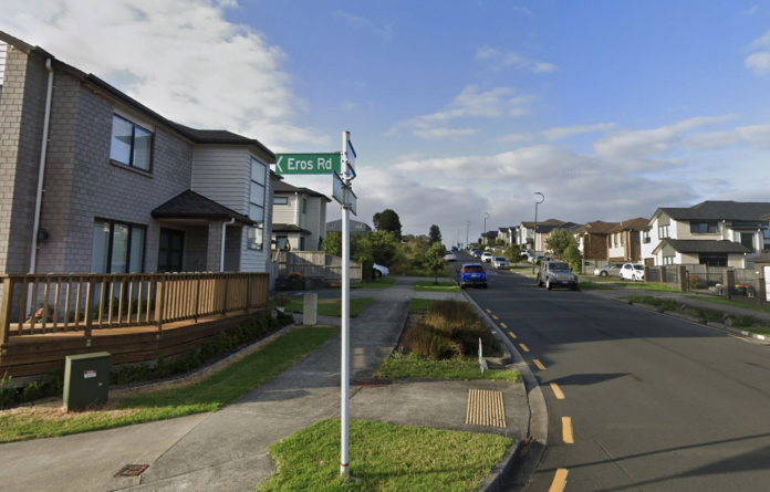 A green Eros Rd street sign at a corner in Flat Bush, with two-storey houses lining the road behind it