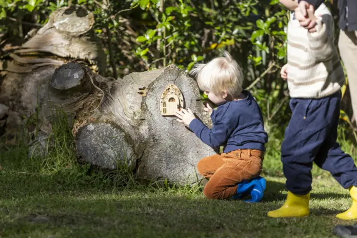 A young child crouches to open a small fairy door built into a mossy log at Howick Historical Village.
