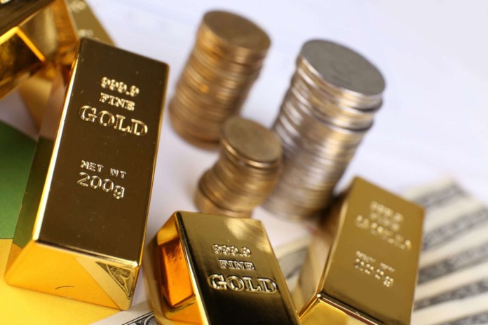 Gold bullion bars and stacked gold and silver coins resting on US banknotes