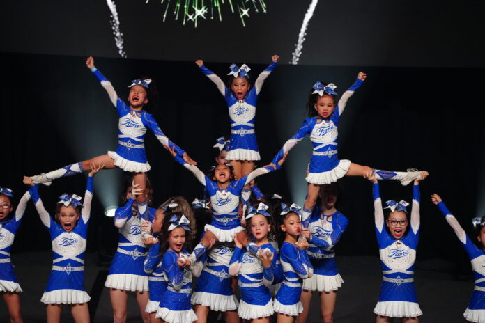 All Star Fame's Duchess cheerleaders in blue and white uniforms performing a stunt routine on stage, with three flyers held aloft.