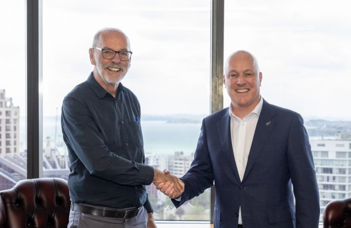 Auckland Mayor Wayne Brown and Christopher Luxon shake hands in an office overlooking Auckland's harbour.