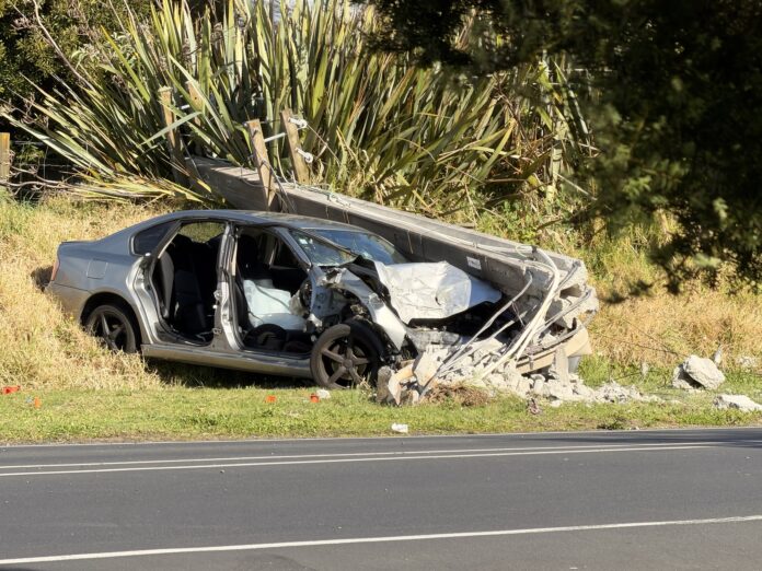 A silver sedan with its right-side doors removed sits on the grass verge of Murphys Road, Flat Bush, with a concrete utility pole lying across its crushed bonnet.